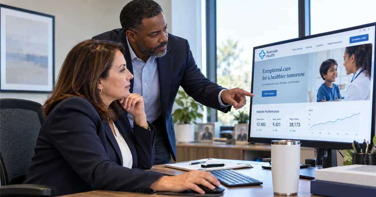 Two healthcare marketing professionals review a provider website and website traffic analytics on a desktop monitor in a modern office.
